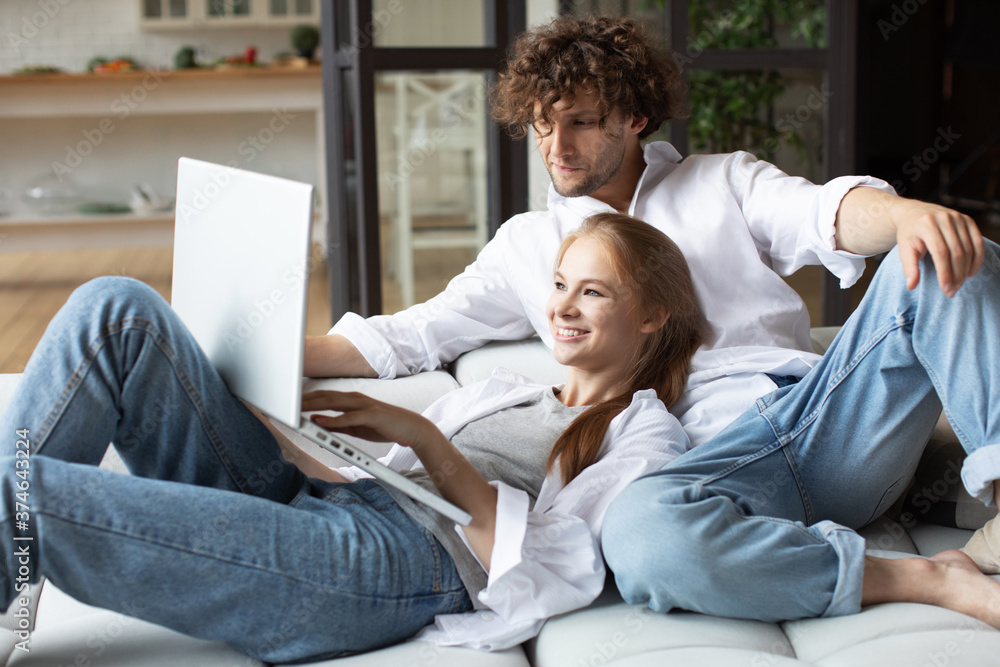 Young couple ordering online, looking in laptop while sitting on couch. Young couple ordering online, looking in laptop while sitting on couch.