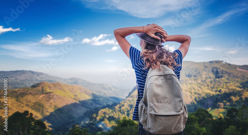 Young female traveler with a backpack and in a hat admiring enjoying the beautiful mountain landscape, travel and freedom lifestyle photo