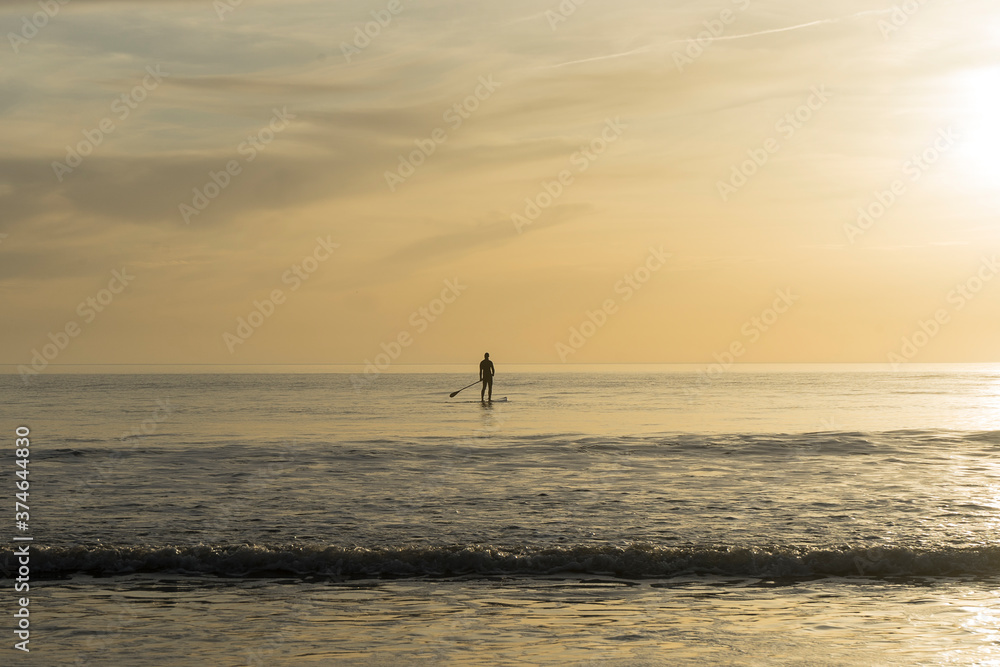 person doing paddle surfing in the sea during the sunset person doing paddle surfing in the sea during the sunset