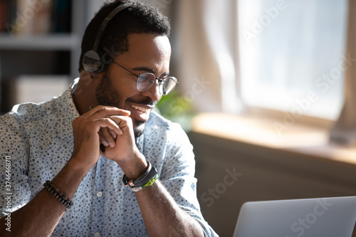 Smiling African American man wearing headphones speaking close up, using laptop, looking at screen, teacher holding online lesson, friendly call center customer service operator consulting client