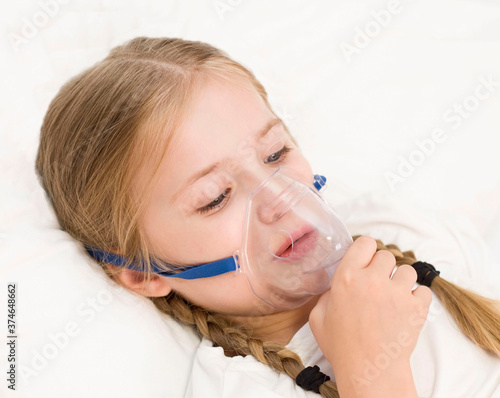 girl is breathing through an inhaler. a sick child is lying on the bed