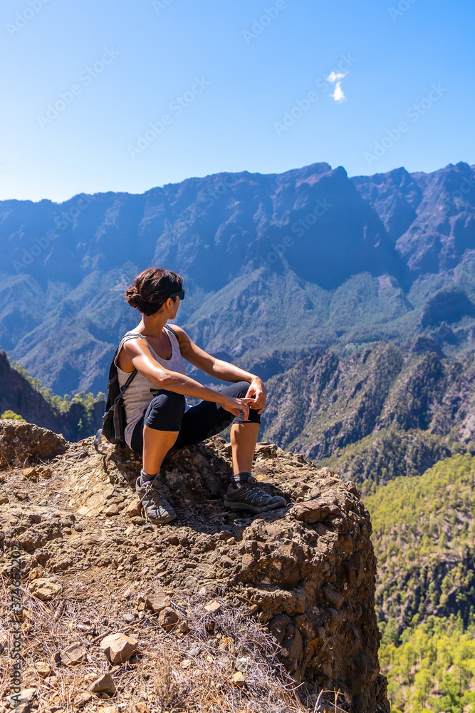 A young woman resting after trekking on top of La Cumbrecita sitting in the natural viewpoint looking at the mountains of the Caldera de Taburiente, La Palma island, Canary Islands, Spain