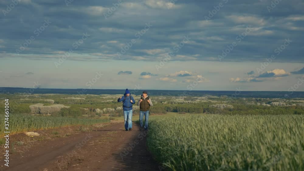 teamwork travel. two man hikers with backpacks walk along a trail next to a field with green grass in nature. lifestyle concept adventure travel hiking healthy. two tourists walk walking talking teamwork travel. two man hikers with backpacks walk along a trail next to a field with green grass in nature. lifestyle concept adventure travel hiking healthy. two tourists walk walking talking