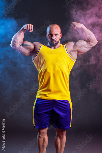 Powerful muscular man posing in the studio with red and blue smoke. Biceps contraction