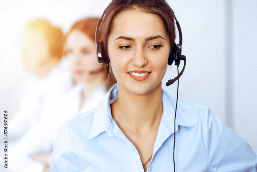 Call center operators. Focus on beautiful business woman using headset in sunny office Call center operators. Focus on beautiful business woman using headset in sunny office
