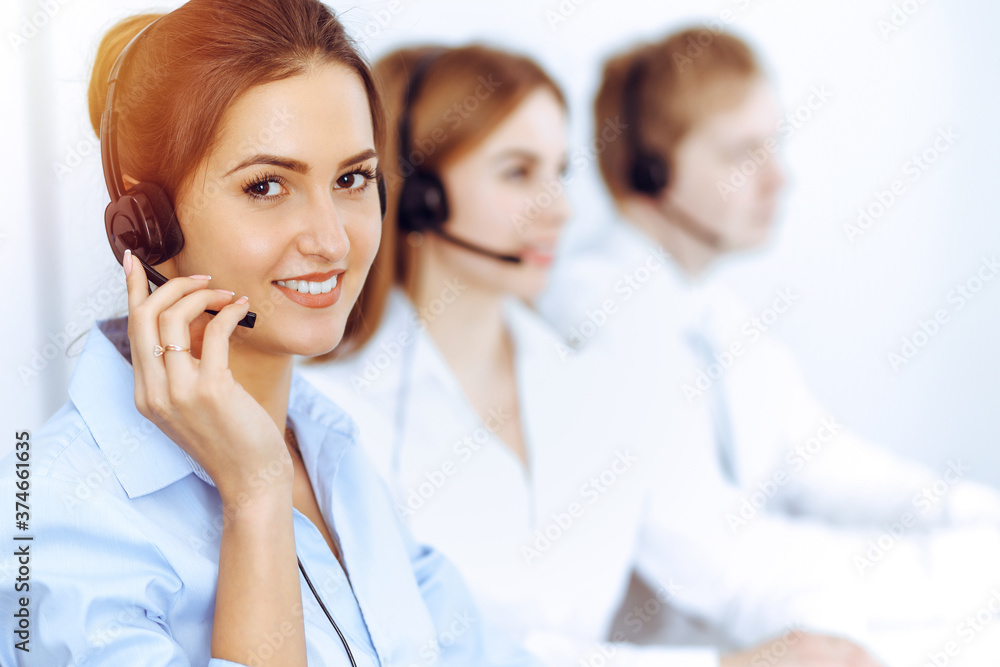 Call center operators. Focus on beautiful business woman using headset in sunny office Call center operators. Focus on beautiful business woman using headset in sunny office