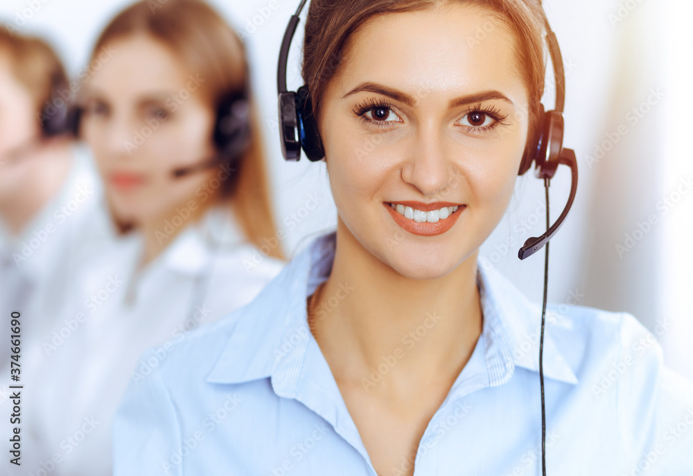 Call center operators. Focus on beautiful business woman using headset in sunny office Call center operators. Focus on beautiful business woman using headset in sunny office