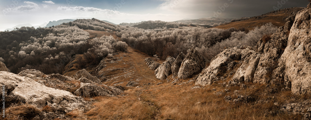 horizontal panorama of the tourist trail and eroded mountain ridge against the background of frosty trees, dramatic sky and hills on the plateau in the distance
