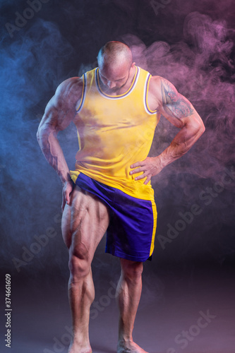 Powerful muscular man posing in the studio with red and blue smoke. Quadriceps contraction