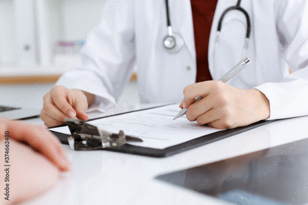 Unknown woman-doctor filling up an application form while consulting patient. Medicine concept Unknown woman-doctor filling up an application form while consulting patient. Medicine concept
