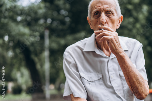 Senior adult men smoking cigarette outdoors in the city park when sitting on the bench.