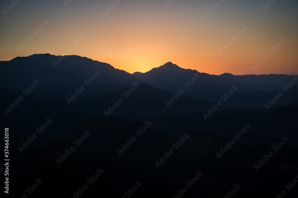 Fototapeta premium Mystical sunset in the Himalayas. The sun has already set behind the top and gilded the sky, while darkness has already descended into the valley and divided the picture into two opposites.