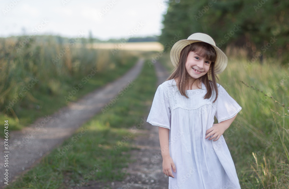 Happy little girl on the road. Cute girl in a white dress stands near field