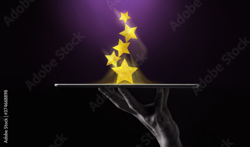 Success in Business or Personal Talent Concept. Hand Raise Up a Digital tablet with Golden Five Star Awards photo