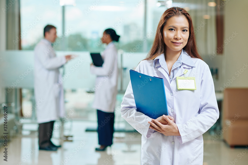 Portrait of positive young medical nurse with clipboard smiling and looking at camera