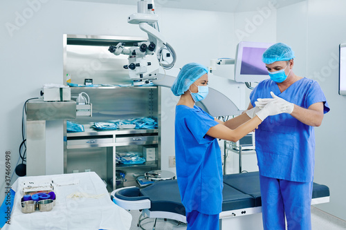 Medical nurse helping ophthalmic surgeon to put on rubber gloves before surgery