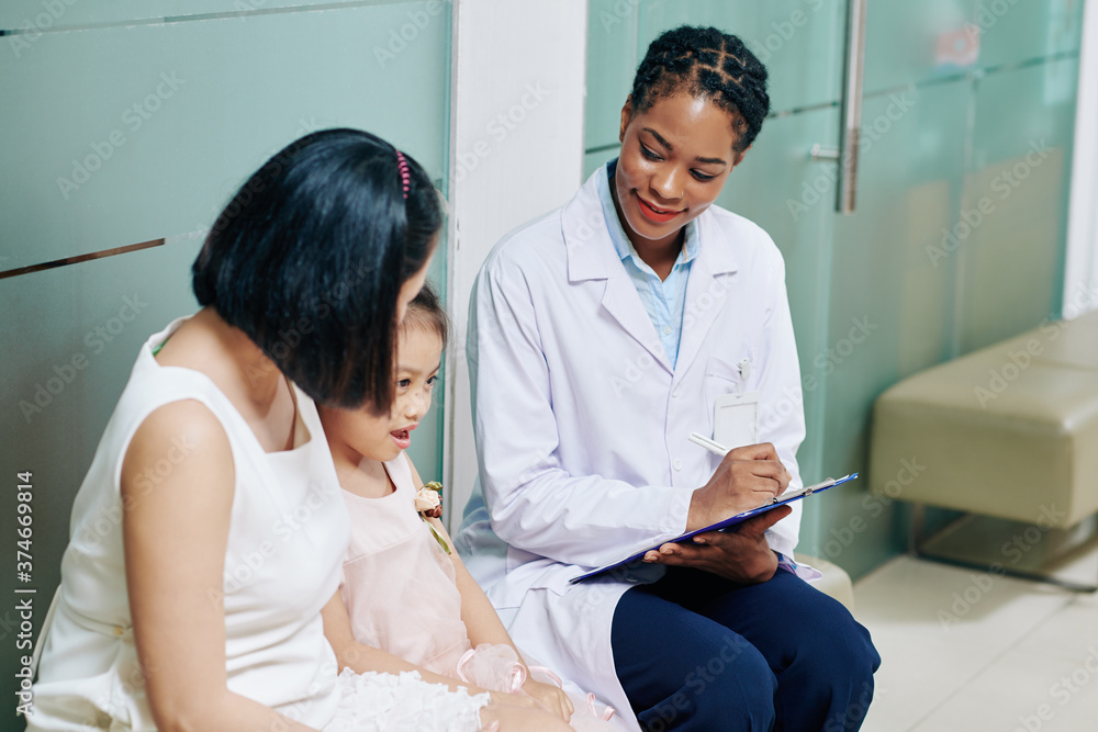 Φωτογραφία Smiling young female pediatrician talking to little girl and her mother and taki