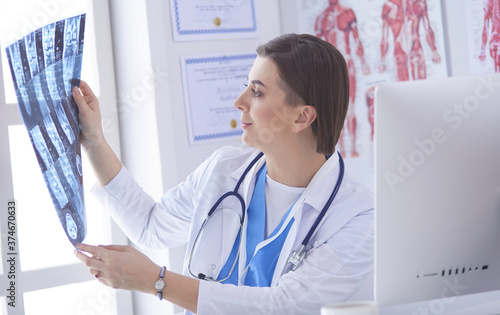 Portrait of doctor sitting in office holding xray image, working on computer photo