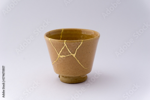 Kintsugi beige sake cup. Gold cracks restoration on old Japanese pottery restored with the antique Kintsugi restoration technique. The beauty of imperfections. 