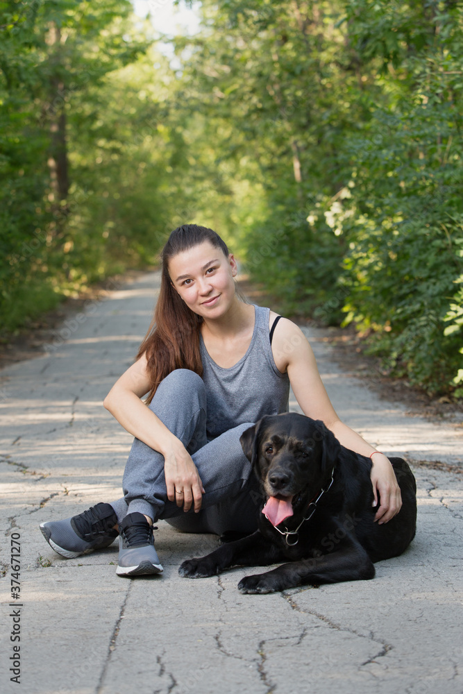 Young attractive sport girl with black Labrador in park. Healthy lifestyle. Walk with favorite pet in wood. Young attractive sport girl with black Labrador in park. Healthy lifestyle. Walk with favorite pet in wood.