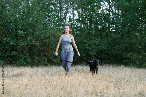 Young attractive sport girl walking with black Labrador in park. Healthy lifestyle. Walk with favorite pet in wood. © jonnyslav