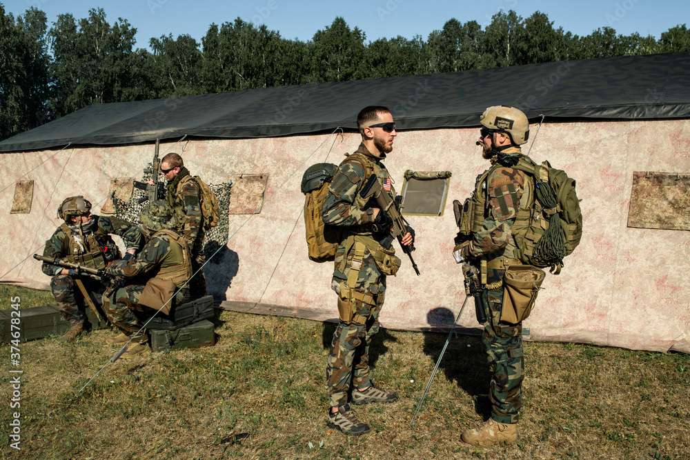 Officer with rifle preparing soldier for military operation and giving advice to him at military base Officer with rifle preparing soldier for military operation and giving advice to him at military base