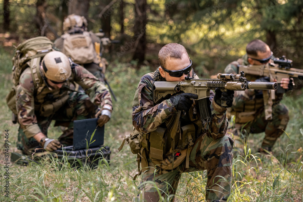 Concentrated snipers sitting on ground and looking through rifle scopes while protecting hacker from enemy in forest Concentrated snipers sitting on ground and looking through rifle scopes while protecting hacker from enemy in forest
