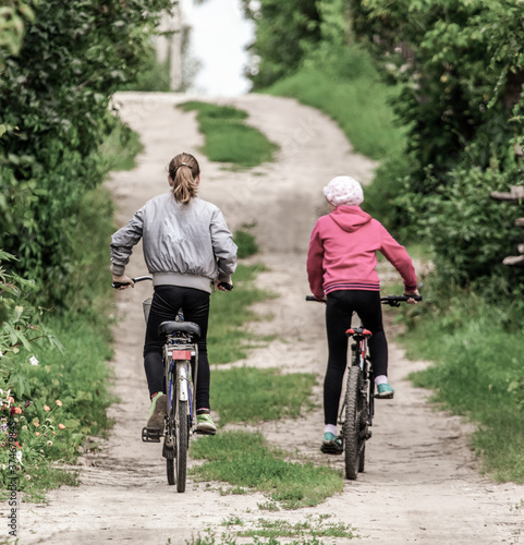 Two girls ride bicycles on a dirt road