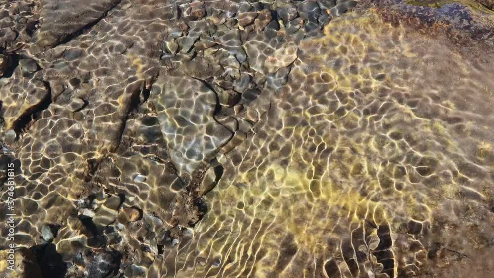 Reflection of sunshine on water with pebble stone on ground. Clean water surface with moving wave of golden reflecting sunlight.