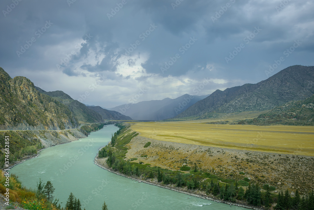 Majestic mountain landscape on a rainy summer or autumn day. Beautiful view of the bend of Katun river, plains and rocks. Torrents of rain, overcast sky. Natural backgrounds.