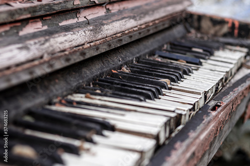 Old broken red piano with peeled paint from rain and wind, outside on an autumn day. Discarded unnecessary musical instrument.