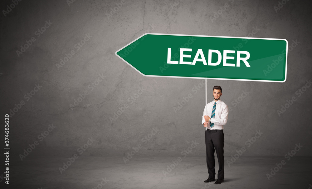 Obraz premium Young business person in casual holding road sign with LEADER inscription, new business direction concept