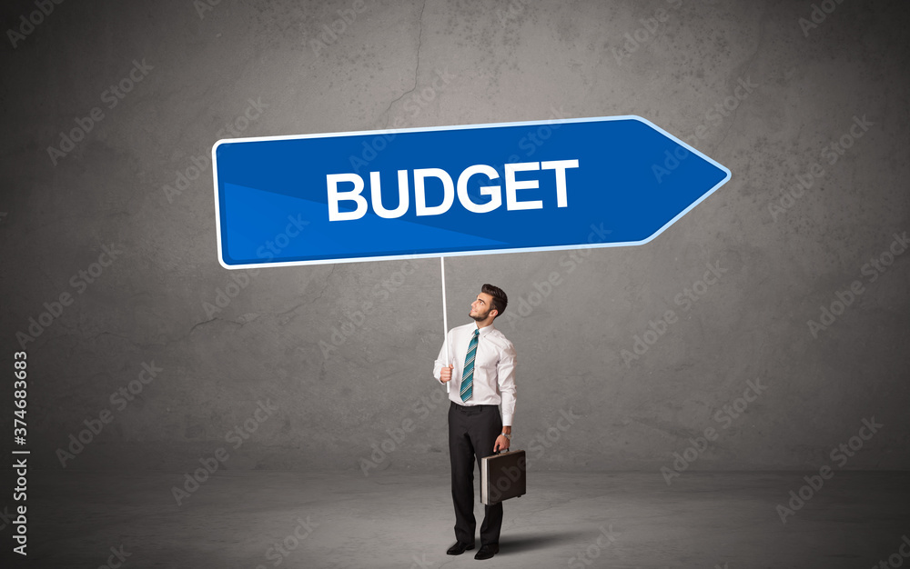 Young business person in casual holding road sign with BUDGET inscription, new business direction concept Young business person in casual holding road sign with BUDGET inscription, new business direction concept