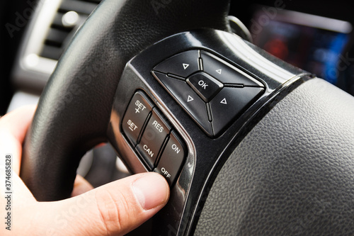 Male driver controls the settings of his car with buttons on the steering wheel. The man's hand on the steering wheel, fingers are pressing the control buttons of cruise control