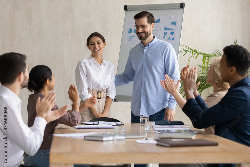 Smiling male leader praising happy millennial arab colleague at group meeting. Smiling diverse coworkers applauding, supporting new worker or congratulating with personal professional achievement.