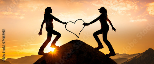 silhouette von zwei Frauen mit einem Herz auf einem Berggipfel