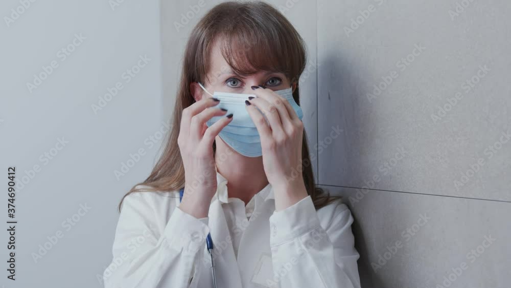 Covid-19 - Portrait of young female doctor in medical virus mask. Woman put on face mask, wearing white medical lab coat standing against gray wall. Covid-19 - Portrait of young female doctor in medical virus mask. Woman put on face mask, wearing white medical lab coat standing against gray wall.