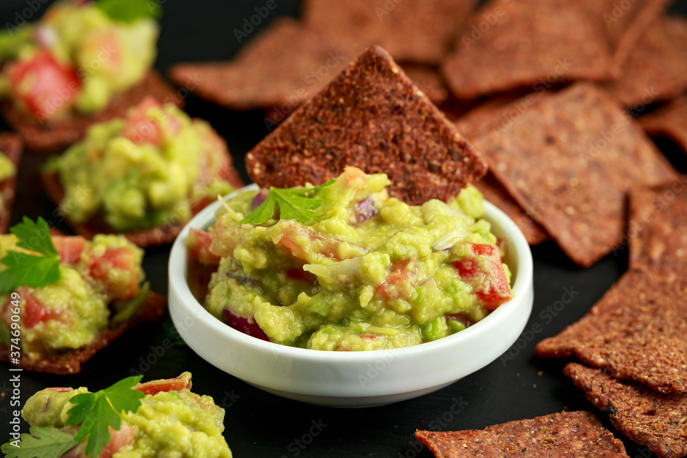 Avocado Guacamole with chipotle and poblano whole grain tortilla chips on rustic stone board Avocado Guacamole with chipotle and poblano whole grain tortilla chips on rustic stone board