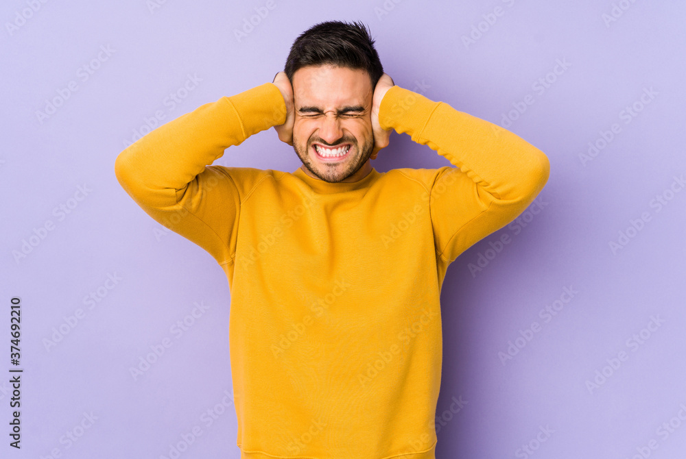 Young caucasian man isolated on purple background covering ears with hands trying not to hear too loud sound. Young caucasian man isolated on purple background covering ears with hands trying not to hear too loud sound.