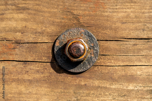 Rusty corroded nut with a washer on a threaded bolt on an old cracked worn wooden surface