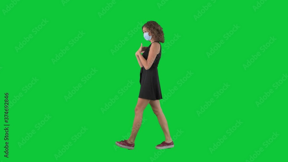 Social distance corona virus prevention concept. Young woman walking wearing protective face mask greeting with elbow bump. Full body side view on green screen chroma key background. Social distance corona virus prevention concept. Young woman walking wearing protective face mask greeting with elbow bump. Full body side view on green screen chroma key background.