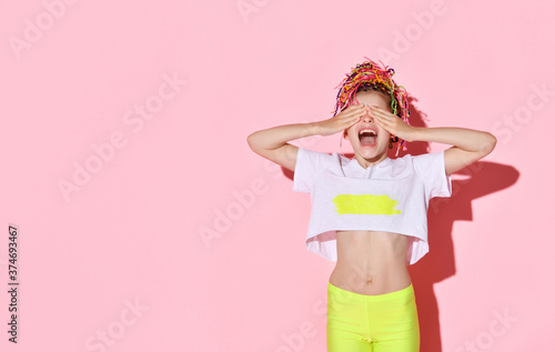 Teenage female with african pigtails has covered her eyes by palms and screaming while posing on pink studio background