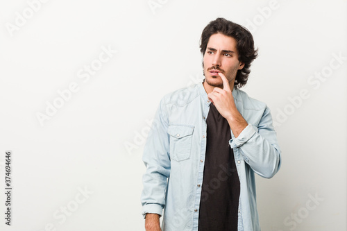 Young handsome man against a white background looking sideways with doubtful and skeptical expression.