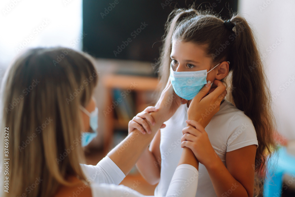 Mother puts on his girl sterile medical mask, protect from infection of virus, pandemic, outbreak and epidemic of disease on quarantine. Life during covid-19 pandemic.