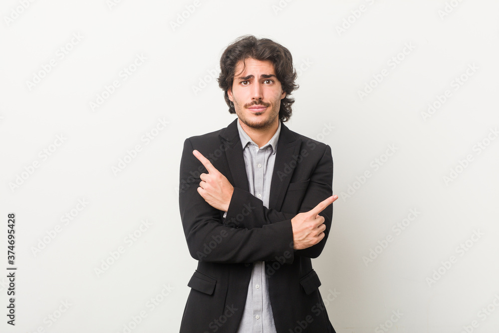 Young business man against a white background points sideways, is trying to choose between two options. Young business man against a white background points sideways, is trying to choose between two options.