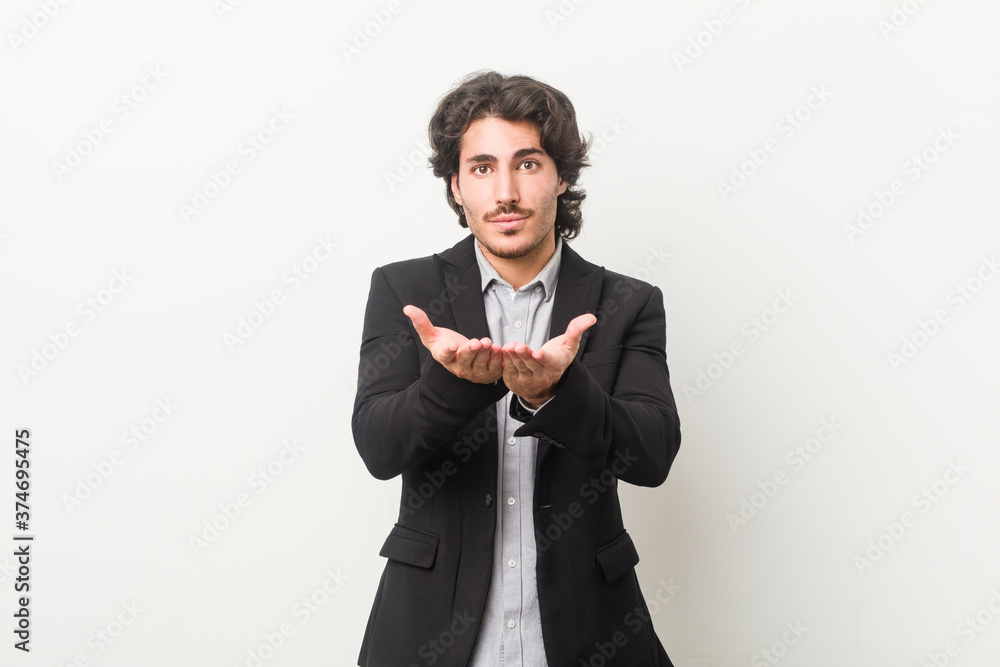 Young business man against a white background holding something with palms, offering to camera. Young business man against a white background holding something with palms, offering to camera.