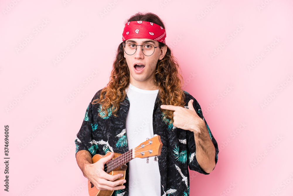 Long hair hippie man holding a ukelele isolated surprised pointing at himself, smiling broadly.
