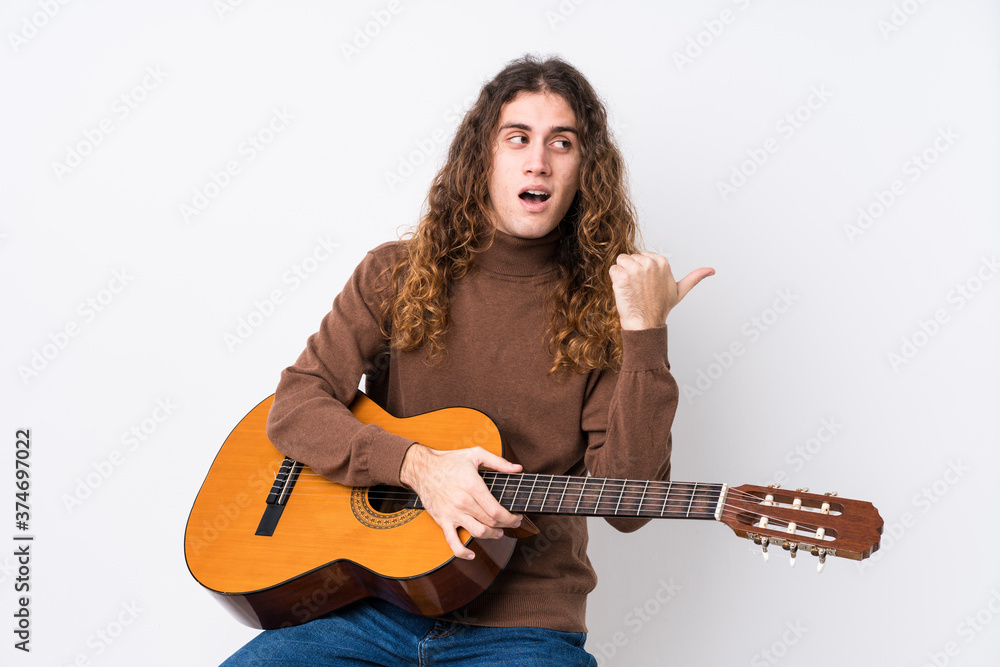 Young caucasian man playing guitar isolated points with thumb finger away, laughing and carefree. Young caucasian man playing guitar isolated points with thumb finger away, laughing and carefree.