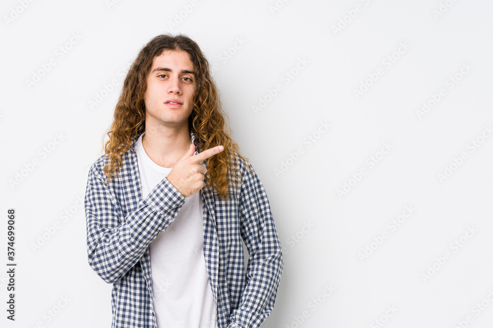 Young long hair man posing isolated smiling and pointing aside, showing something at blank space. Young long hair man posing isolated smiling and pointing aside, showing something at blank space.