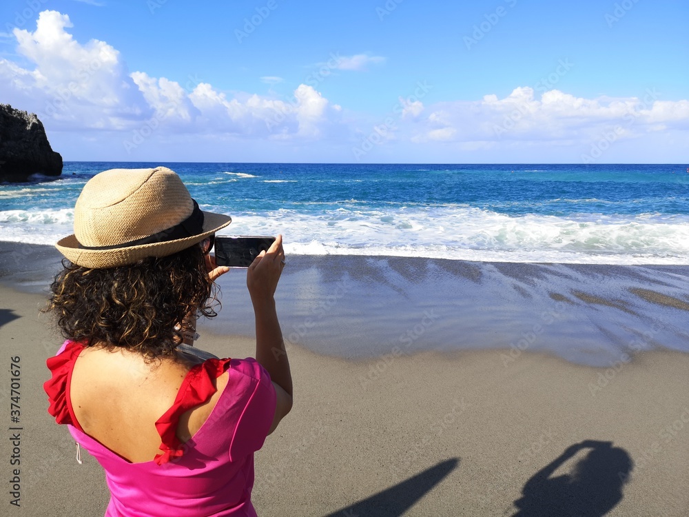 Woman from behind with hat photographing the sea Woman from behind with hat photographing the sea